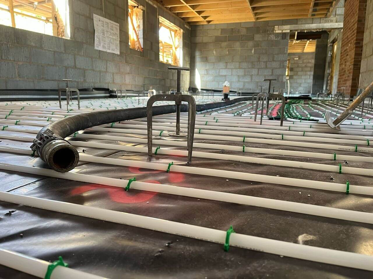 Close up / low down image of white underfloor heating pipes clipped down with green clips