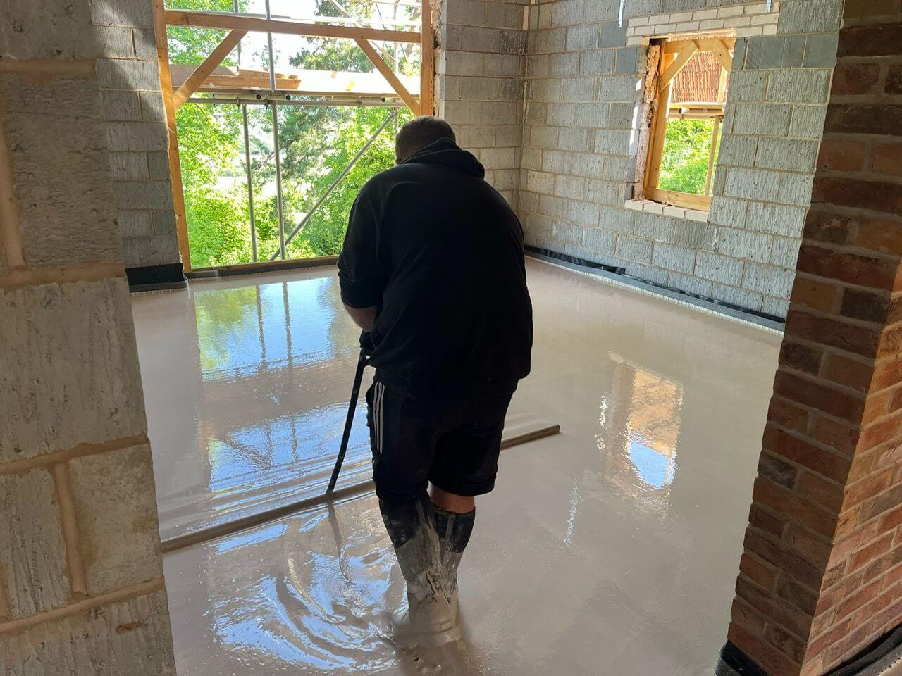 A man levelling out liquid screed in a room