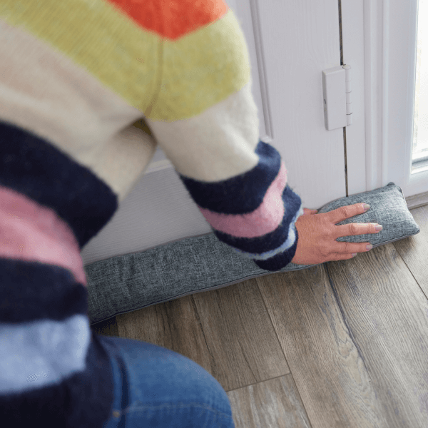 Woman laying draught excluder at door to improve underfloor heating efficiency