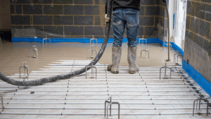 Underfloor heating installer pouring liquid screed over pipes